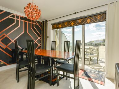 A dining room with black chairs and a wooden table next to glass doors leading to a balcony at 24 Burgh Island Causeway in Bigbury-on-Sea