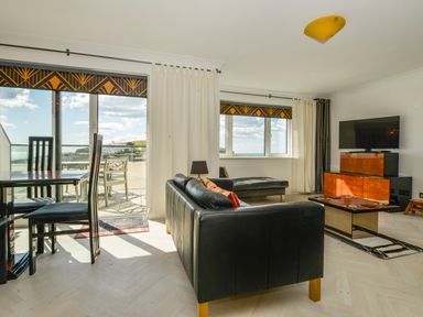 A living room with black leather sofas a dining table with chairs and a television at 24 Burgh Island Causeway in Bigbury-on-Sea