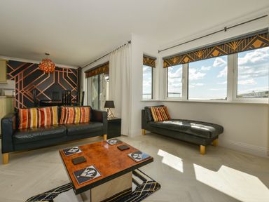 A living room with black leather sofas striped cushions a wooden coffee table and patterned wallpaper at 24 Burgh Island Causeway in Bigbury-on-Sea