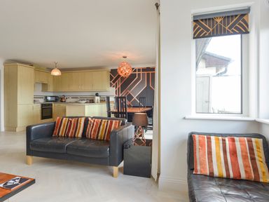An open-plan living room and kitchen area with black leather sofas with striped cushions at 24 Burgh Island Causeway in Bigbury-on-Sea