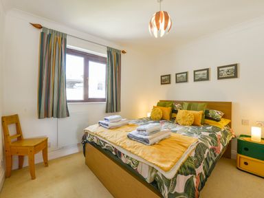 A bedroom with a double bed with patterned and yellow bedding a wooden chair and a small bedside table at 24 Burgh Island Causeway in Bigbury-on-Sea