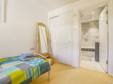 A bedroom with a single bed with folded towels a wooden mirror a closet with sliding doors and a bathroom with marble walls at 24 Burgh Island Causeway in Bigbury-on-Sea