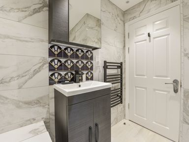 A bathroom with a sink cabinet and mirror above next to a white door and a black towel radiator at 24 Burgh Island Causeway in Bigbury-on-Sea