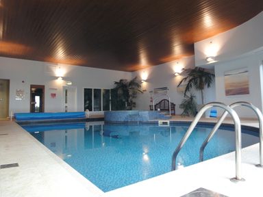 An indoor swimming pool with tiled walls and floor a hot tub plants and paintings on the walls at 24 Burgh Island Causeway in Bigbury-on-Sea