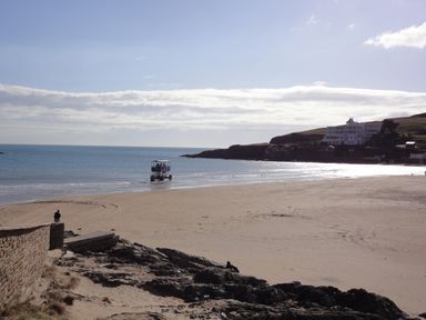 A beach with a person near a stone wall and a vehicle in shallow water by the sea at 24 Burgh Island Causeway in Bigbury-on-Sea