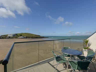 A balcony with a round table and four chairs overlooking a beach and an island at 23 Burgh Island Causeway in Bigbury-on-Sea