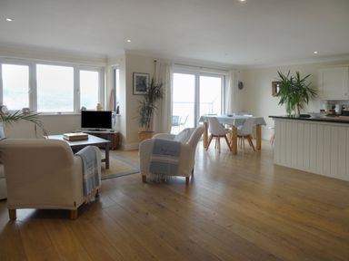 An open living and dining area with white armchairs a coffee table a small TV a dining table with four chairs and plants at 23 Burgh Island Causeway in Bigbury-on-Sea