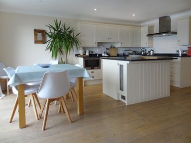 A kitchen with white cabinets a wooden dining table with white chairs and a plant at 23 Burgh Island Causeway in Bigbury-on-Sea