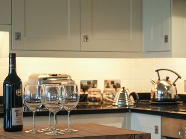 A kitchen counter with a bottle of wine and three wine glasses with a toaster and kettle on the countertop at 23 Burgh Island Causeway in Bigbury-on-Sea