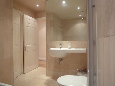 A bathroom with a wall-mounted sink, a toilet, a large mirror, and an open door at 23 Burgh Island Causeway in Bigbury-on-Sea