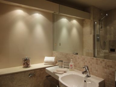 A bathroom sink with folded towels soap and a glass container under wall lights at 23 Burgh Island Causeway in Bigbury-on-Sea