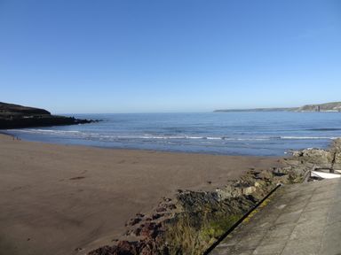 A sandy beach with rocky edges and calm sea under a clear sky at 23 Burgh Island Causeway in Bigbury-on-Sea