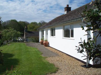 A white house with windows and two large pots near the entrance on a lawn with trees and a picnic table at Orchard View in Kellaton near Hallsands