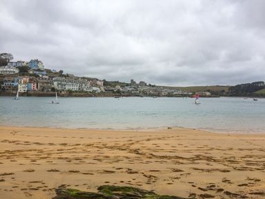 A sandy beach overlooking a body of water with sailboats and a town with multiple houses in the background at Orchard View in Kellaton near Hallsands