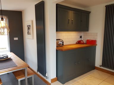 A kitchen area with dark grey cabinets a wooden countertop a red telephone a toaster and a bread box next to a dining table with benches and vertical radiators on the walls at Orchard View in Kellaton near Hallsands