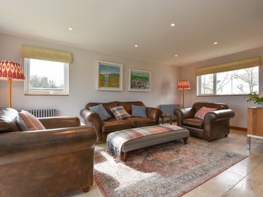 A living room with brown leather sofas a patterned ottoman and paintings on the wall at Orchard View in Kellaton near Hallsands
