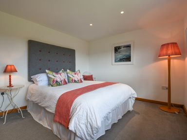 A bedroom with a bed with floral pillows and red accents two lamps and a framed picture on the wall at Orchard View in Kellaton near Hallsands