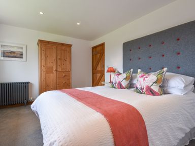 A bedroom with a bed with white bedding and floral pillows a wooden wardrobe and a wooden door at Orchard View in Kellaton near Hallsands
