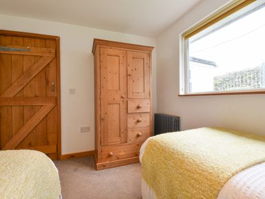A bedroom with two single beds a wooden wardrobe a wooden door and a window at Orchard View in Kellaton near Hallsands