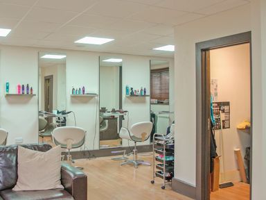 A salon room with styling chairs mirrors shelves with hair products and a leather sofa at Mixit Cottage in Kingsbridge