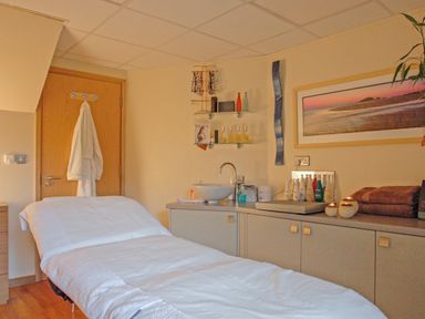 A treatment room with a massage table towels candles and skincare products at Mixit Cottage in Kingsbridge