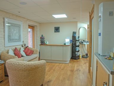 A waiting area with wicker chairs and a sofa with cushions next to a reception desk with a nail polish display at Mixit Cottage Kingsbridge