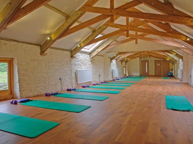 A yoga or exercise room with green mats and purple weights on a wooden floor with exposed wooden beams on the ceiling at Mixit Cottage in Kingsbridge