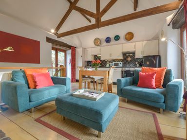 A living area with two blue armchairs and a matching ottoman in front of a wooden dining table and kitchen at Mixit Cottage in Kingsbridge