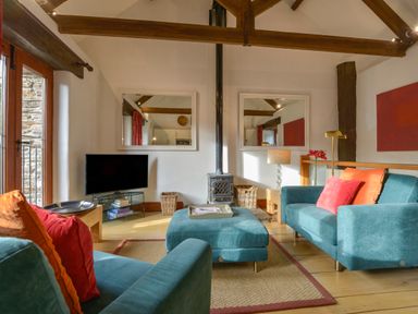 A living room with blue sofas and orange pillows a television and a wood burning stove at Mixit Cottage in Kingsbridge