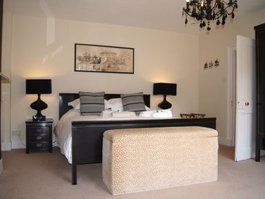 A bedroom with a black bed frame two bedside tables with lamps and a beige ottoman at Maristow Barton in Milton Combe near Lopwell Dam