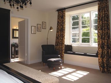 A bedroom with a chair and ottoman near a window seat with cushions and patterned curtains at Maristow Barton in Milton Combe near Lopwell Dam