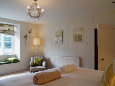 A bedroom with a bed with rolled towels pillows an armchair near a window and a chandelier at Maristow Barton in Milton Combe near Lopwell Dam