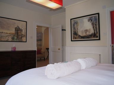A bedroom with a bed and rolled towels a wooden dresser and framed paintings at Maristow Barton in Milton Combe near Lopwell Dam