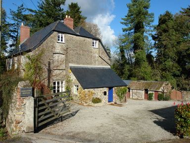 A stone house with a black roof and blue door next to wooden gate and outbuildings surrounded by trees at Maristow Barton in Milton Combe near Lopwell Dam