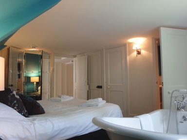 A bedroom with a bed towels and pillows a bathtub and a wall lamp at Maristow Barton in Milton Combe near Lopwell Dam