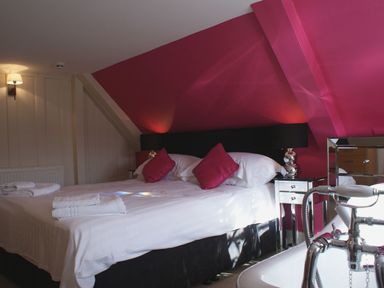A bedroom with a double bed with white linens red cushions and a bathtub with faucet at Maristow Barton in Milton Combe near Lopwell Dam