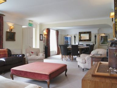 A living room with armchairs and a pink ottoman next to a dining table with black chairs at Maristow Barton in Milton Combe near Lopwell Dam