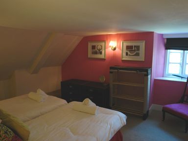 A bedroom with twin beds with rolled towels on them a dresser a shelving unit a window and a chair at Maristow Barton in Milton Combe near Lopwell Dam