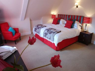 A bedroom with a double bed red armchair flowers and bedside tables with lamps at Maristow Barton in Milton Combe near Lopwell Dam