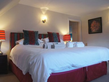A bedroom with a bed with white linens and pillows with a headboard and bedside tables with lamps and a framed flower picture on the wall at Maristow Barton in Milton Combe near Lopwell Dam