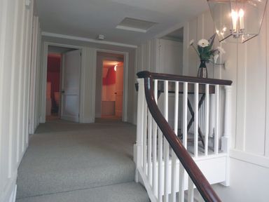 A hallway with carpeted stairs and white wooden railing and a table with flowers at Maristow Barton in Milton Combe near Lopwell Dam