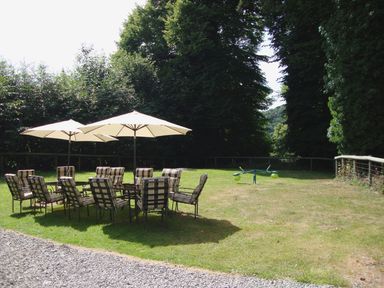 An outdoor grassy area with tables, chairs, umbrellas, and a seesaw at Maristow Barton in Milton Combe, near Lopwell Dam