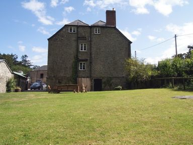 A stone building with multiple windows and a chimney with a lawn and wooden benches in front at Maristow Barton Milton Combe near Lopwell Dam