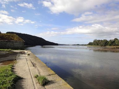 A river with a stone building on the left and trees along the shore at Maristow Barton in Milton Combe near Lopwell Dam