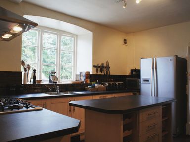 A kitchen with wooden cabinets black countertops a silver refrigerator and a window showing trees at Maristow Barton in Milton Combe near Lopwell Dam