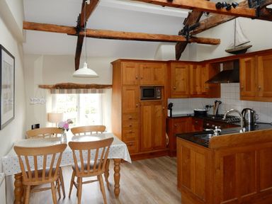 A kitchen with wooden cabinets dining table with four chairs and exposed wooden beams at Cherry Tree Cottage in Noss Mayo