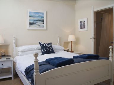 A bedroom with a white wooden bed and blue towels on top with bedside tables and lamps at Cherry Tree Cottage in Noss Mayo