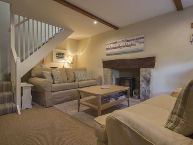 A living room with two sofas a coffee table a fireplace and stairs at Cherry Tree Cottage in Noss Mayo