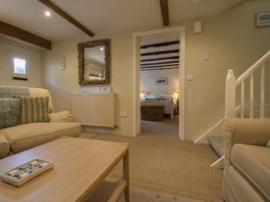 A living room with sofas and a wooden table with a tray leading to a bedroom at Cherry Tree Cottage in Noss Mayo