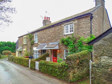 A stone cottage with moss-covered walls and plants along a narrow road at 1 Gabberwell Cottages in Kingston